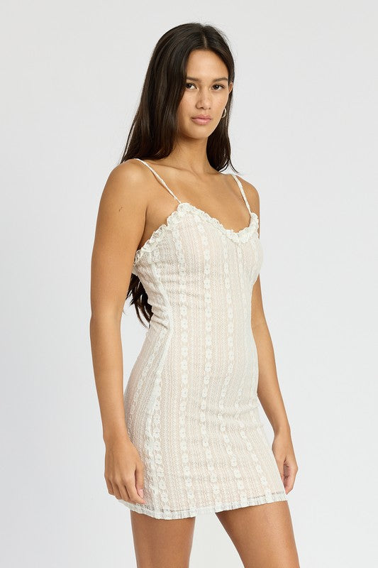 Woman wearing a white lace ruffled trimmed v-neck mini dress against a plain background side view