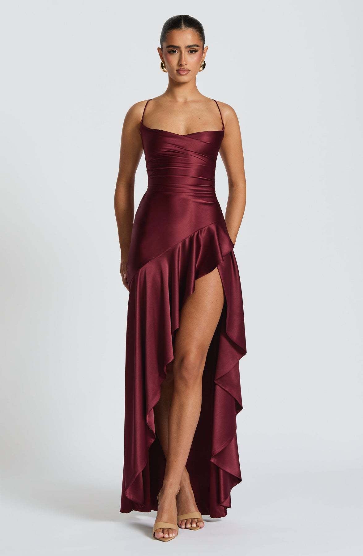 Woman wearing a burgundy evening backless gown with a high slit on a white background