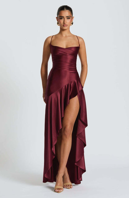 Woman wearing a burgundy evening backless gown with a high slit on a white background