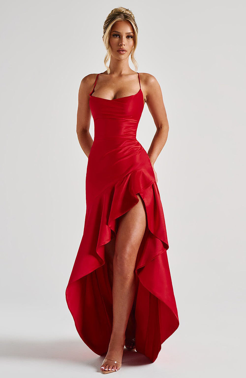 Woman wearing a red maxi backless dress with a high-low hem on a white background