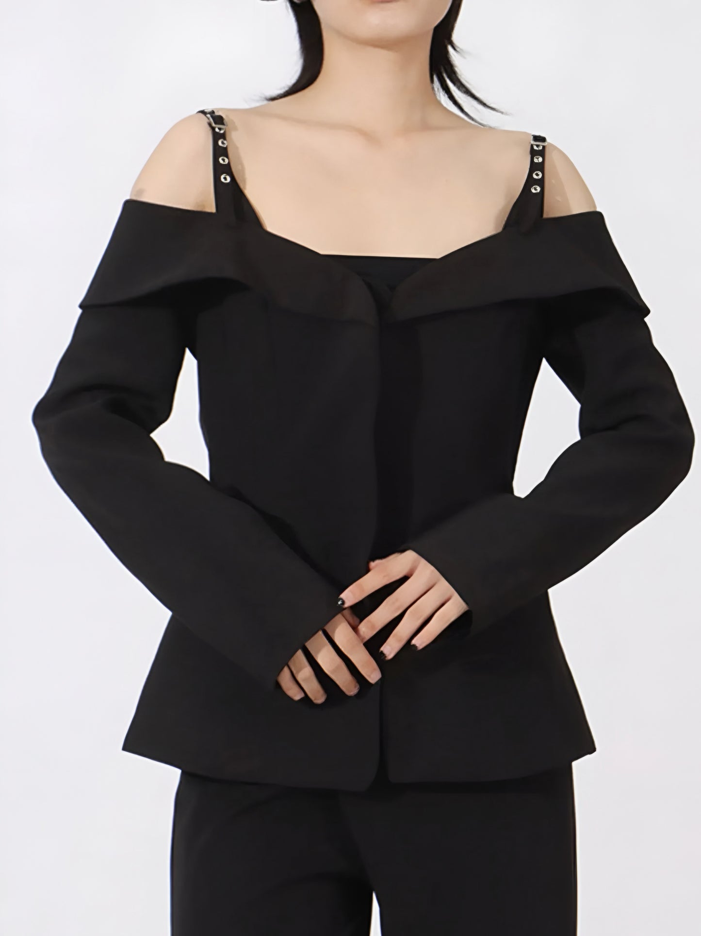 Woman wearing a designer inspired black ruffled cold shoulder blazer with buckle straps on a white background