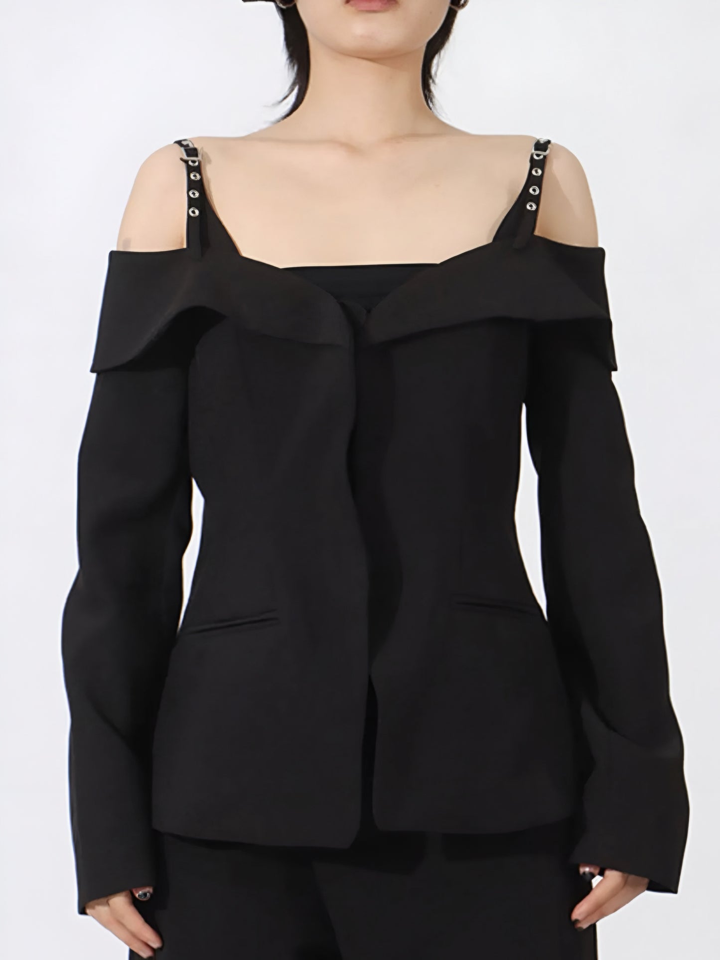Woman posing in a black luxury designer inspired fashion cold-shoulder blazer/jacket with buckle strap and ruffled details on a white background