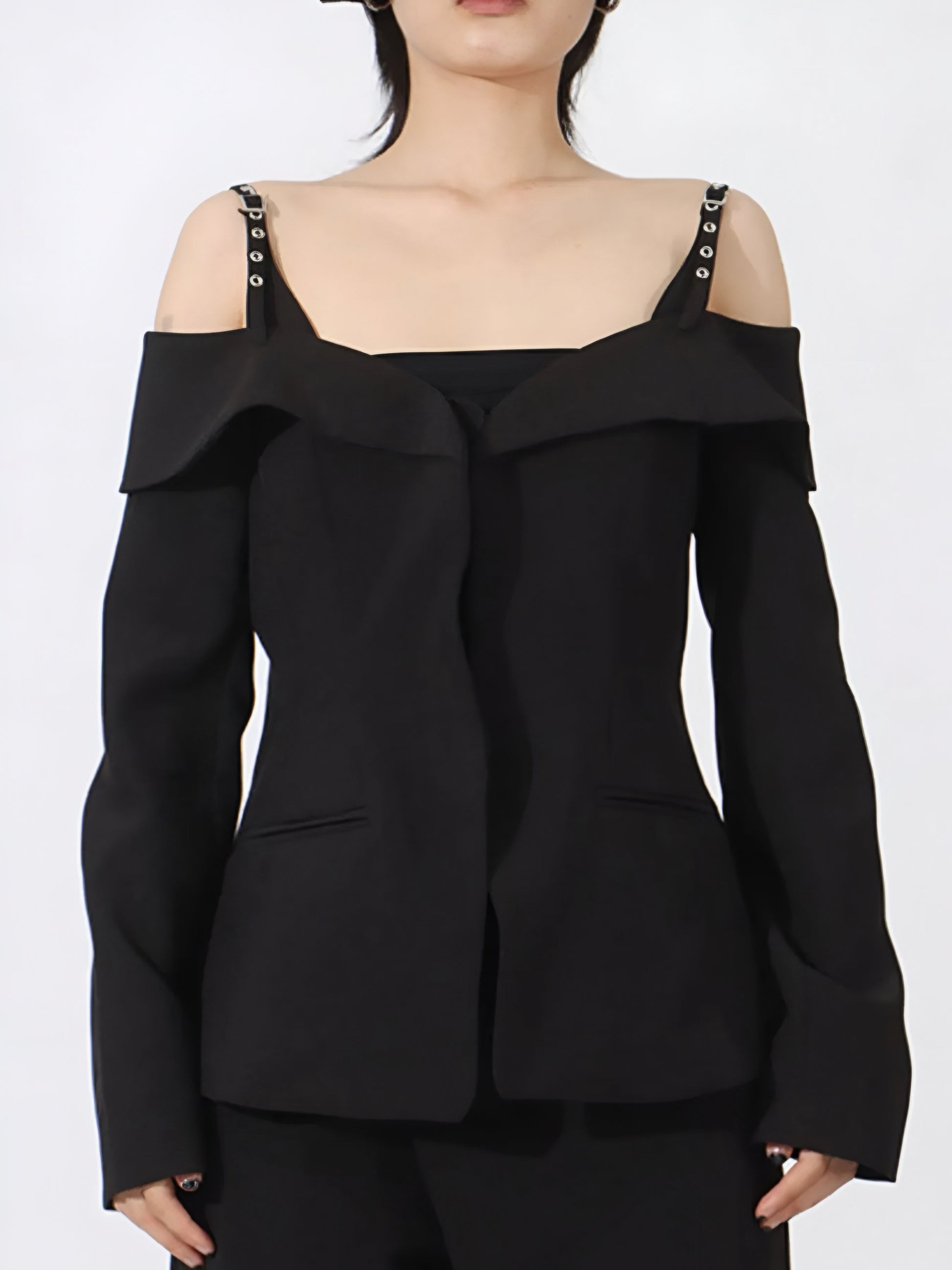 Woman posing in a black luxury designer inspired fashion cold-shoulder blazer/jacket with buckle strap and ruffled details on a white background