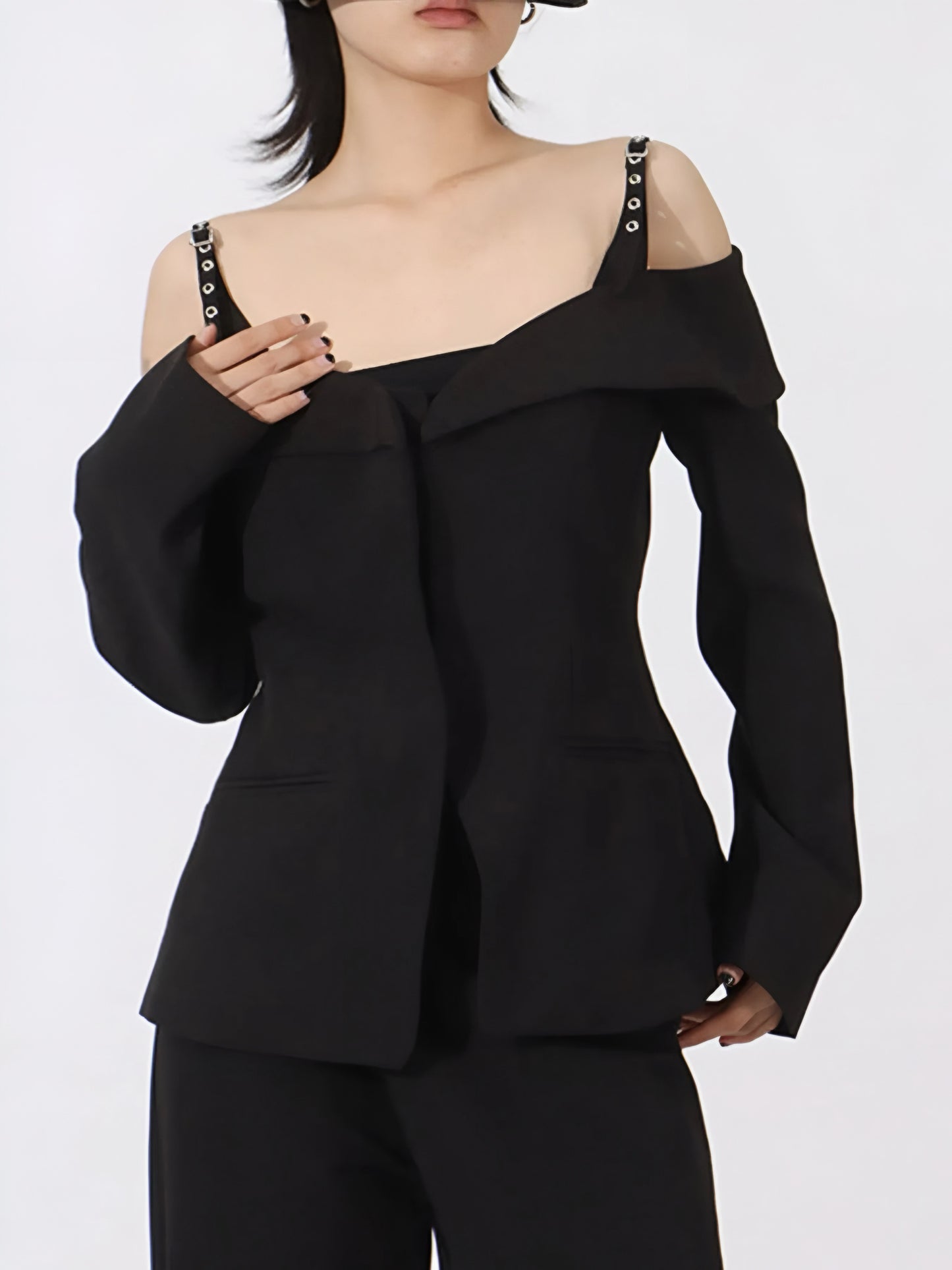 Woman wearing a black luxury designer inspired fashion cold-shoulder blazer/jacket with edgy statement buckle strap  on a white background