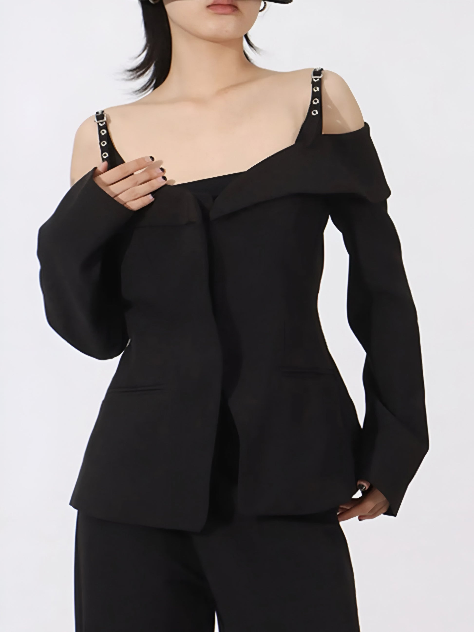 Woman wearing a black luxury designer inspired fashion cold-shoulder blazer/jacket with edgy statement buckle strap  on a white background
