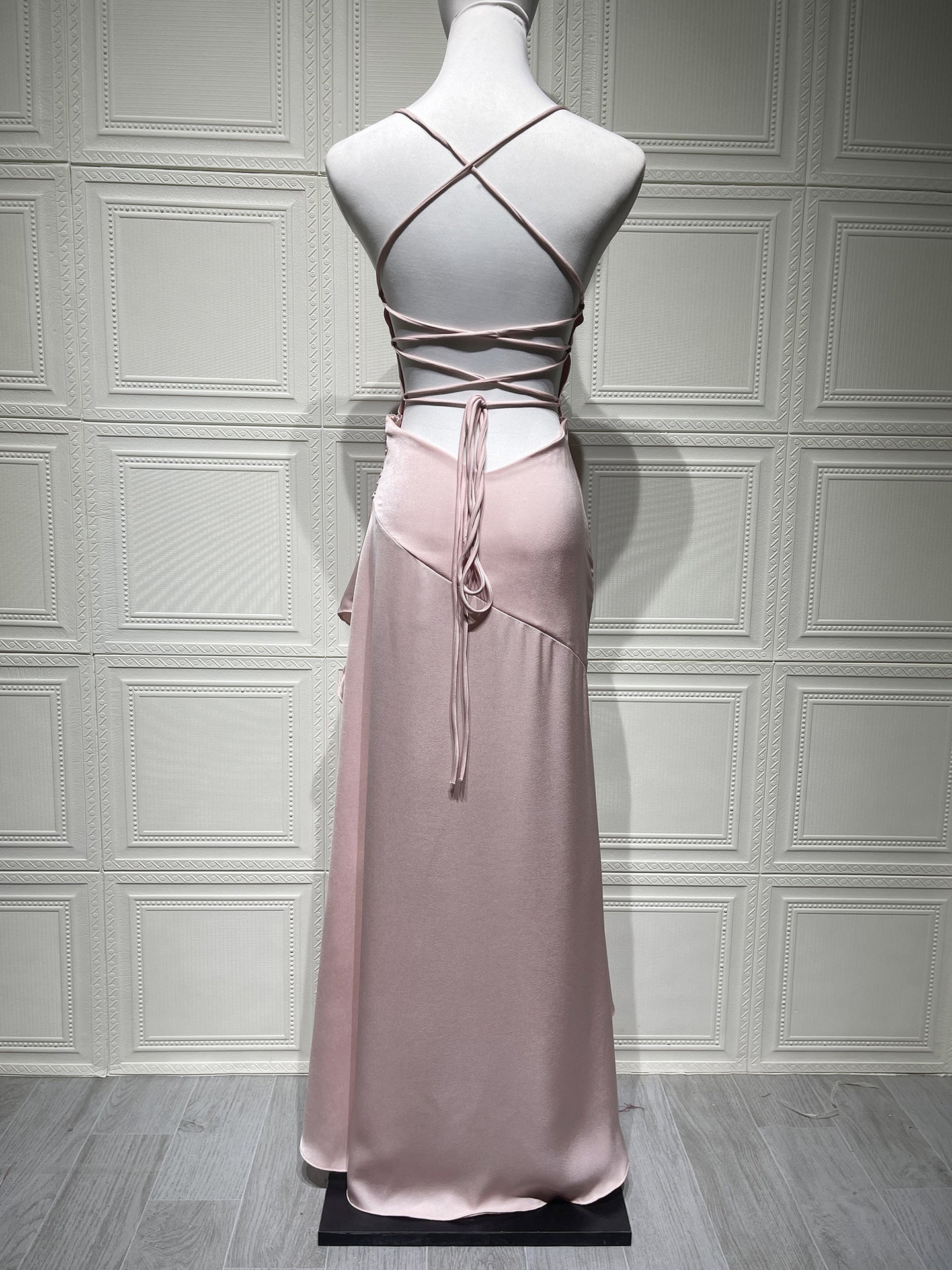 Mannequin wearing a pink dress with criss-cross backless design on a gray paneled wall background