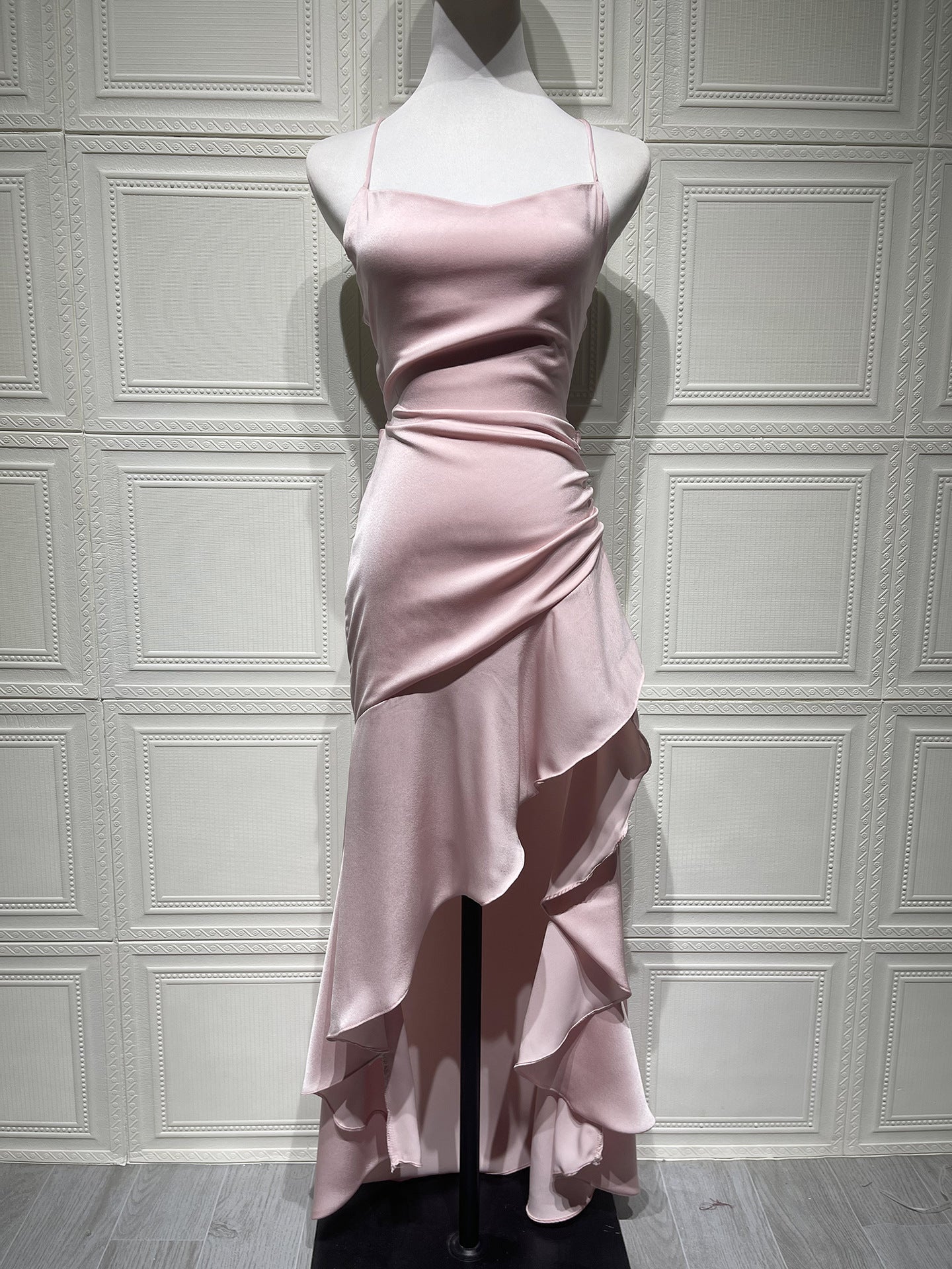 Pink evening gown on a mannequin against a white paneled wall.