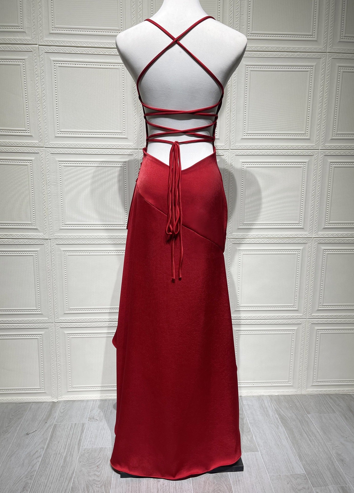 Red backless evening gown on a mannequin against a white paneled wall