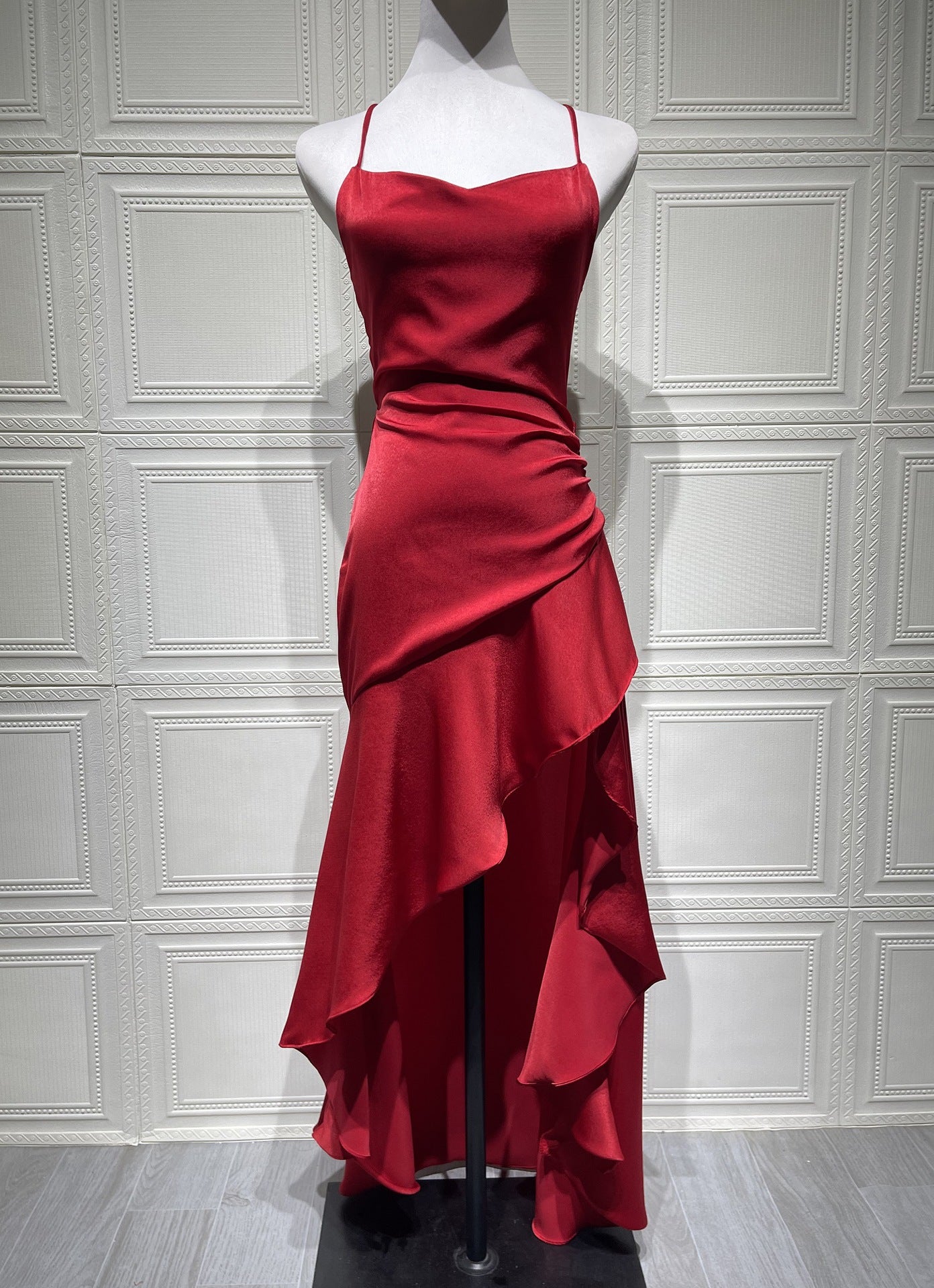 Red evening gown on a mannequin against a white paneled wall.