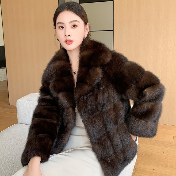 Woman wearing a brown elegant cruelty-free faux mid length fur winter coat sitting on a chair