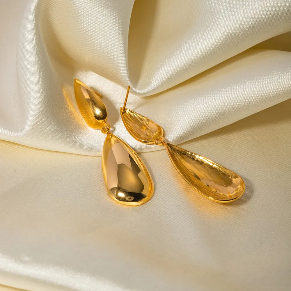 Gold sculptural dangle drop earrings on a cream satin fabric background

