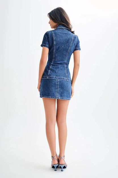 back view of woman wearing a two piece dark wash denim short sleeve top and mini skirt casual set on a white background