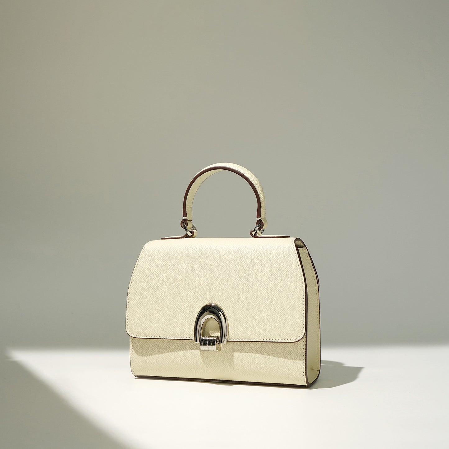 An ivory/white colored handbag with a shell shape, made from genuine leather, featuring a sandwich pocket design and a single handle strap.