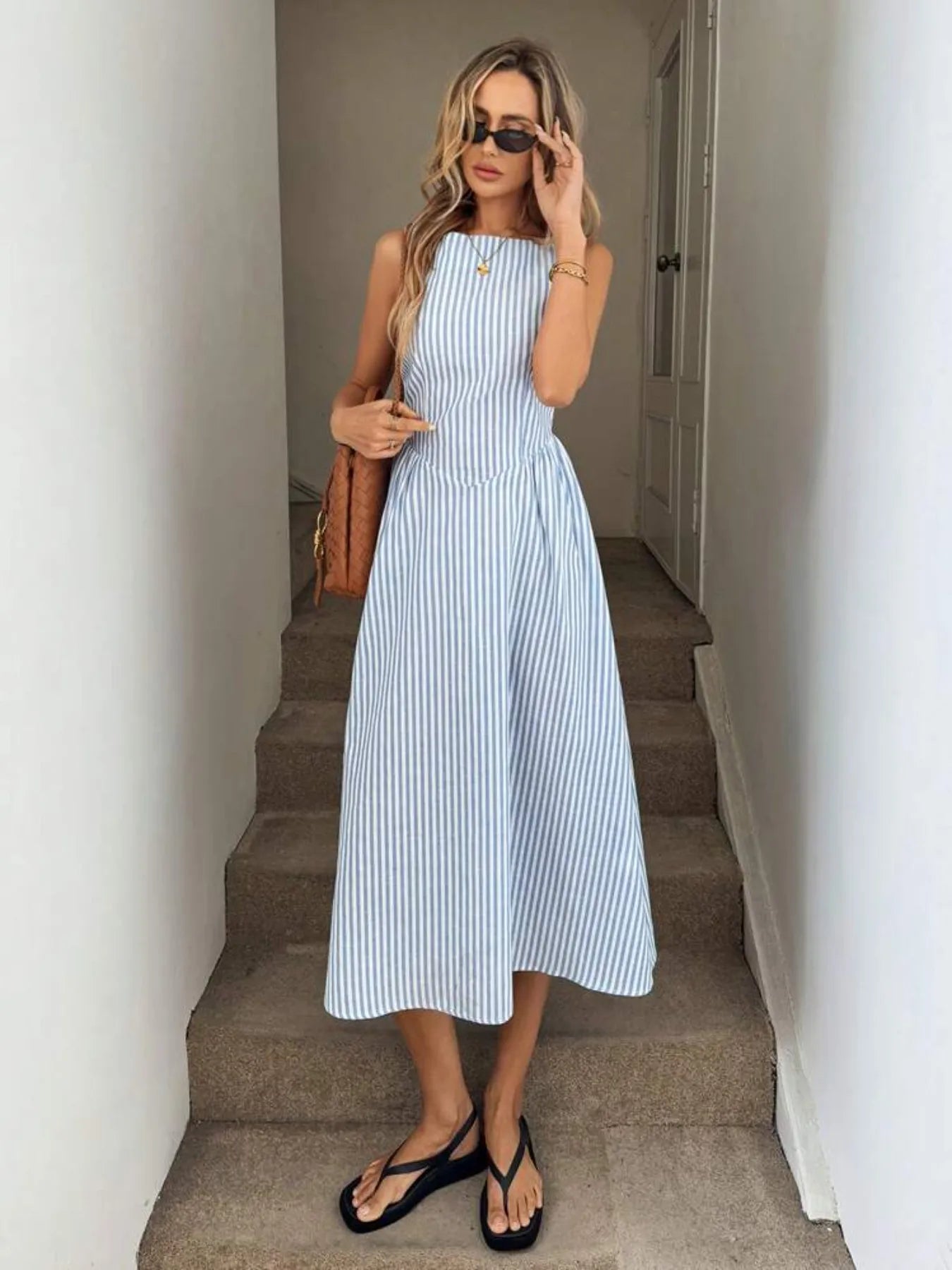 Woman wearing blue sleeveless striped midi dress front view holding a shoulder bag