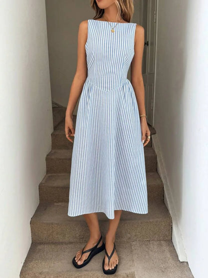 Woman wearing a blue and white striped casual resort style dress standing on a staircase.