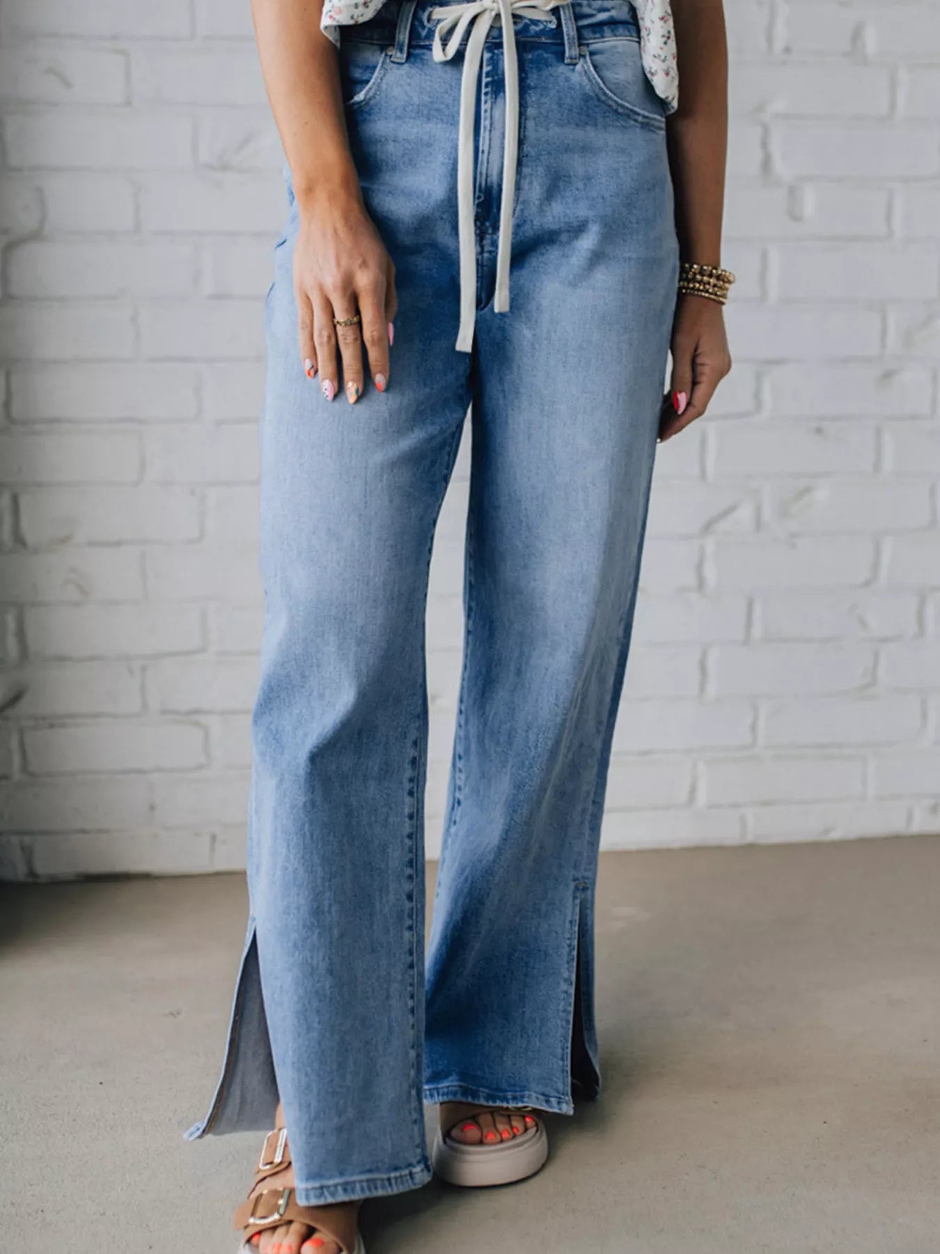 Woman posing in a light blue wash denim  wide-leg high rise jeans against a white brick wall.