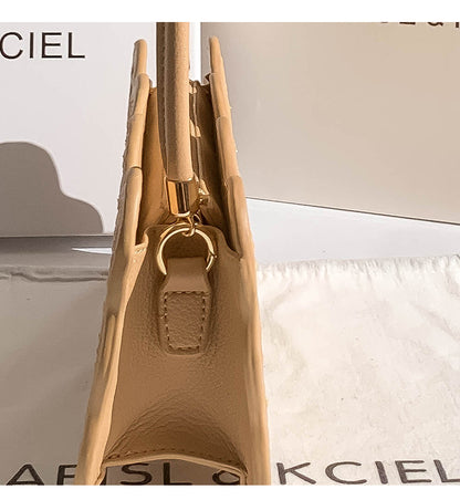 Close-up of a beige handbag with a gold handle and clasp, branded 'Kciel'.