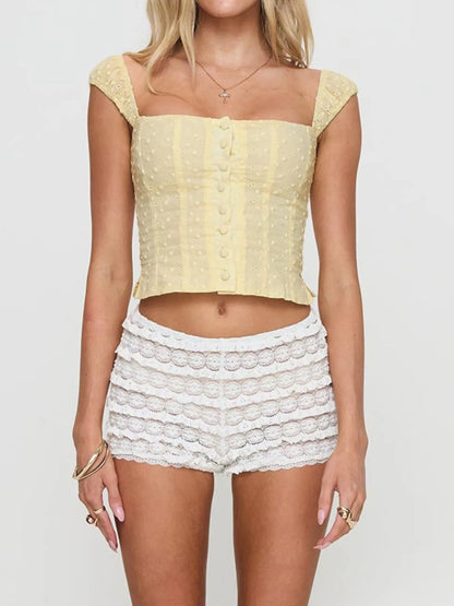 Woman wearing a yellow Smocked  buttoned Square Neck Top top and white lace shorts on a plain background