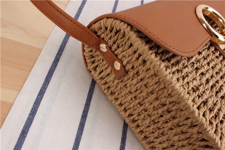 Close up of side of woven straw handbag with brown leather strap and flap on a striped fabric background