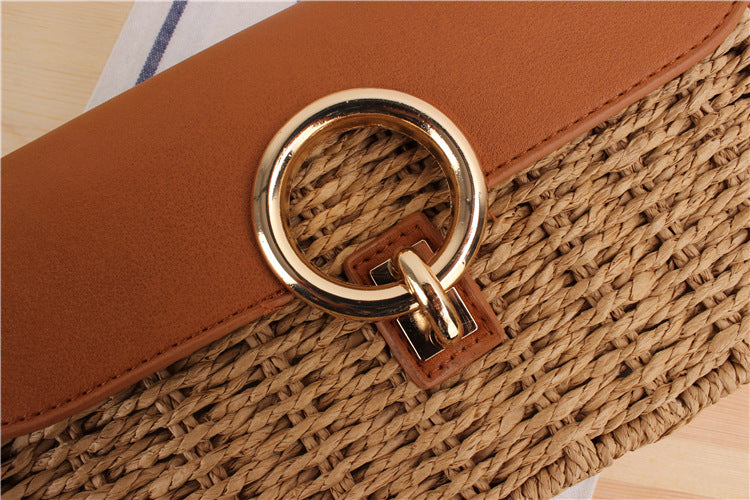 Close-up of a woven straw handbag with a gold ring handle on a wooden surface.