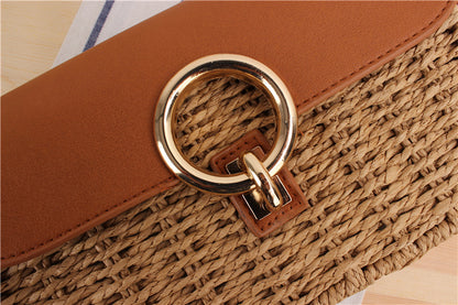 Close-up of a woven straw handbag with a gold ring handle on a wooden surface.