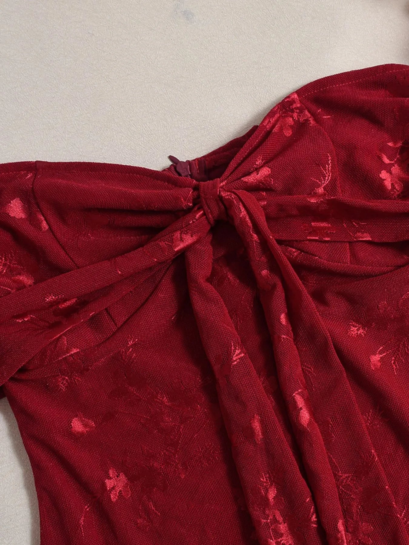 Close-up of neckline for a red Sweetheart Neck Draped Off-Shoulder Bodycon Dress with a bow detail on a neutral background