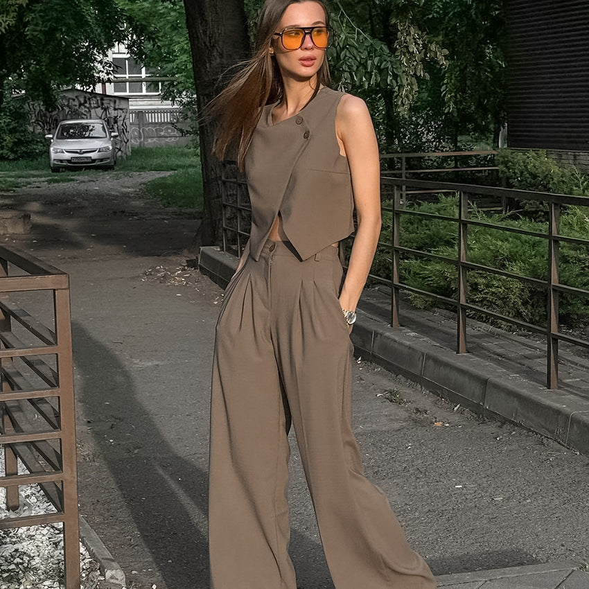 Woman in a brown two piece pant suit set with sleeveless vest  standing outdoors with trees and a car in the background