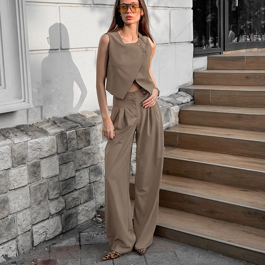 Woman in a brown two piece vest and  pant suit set outfit standing on stone steps with a stone wall background