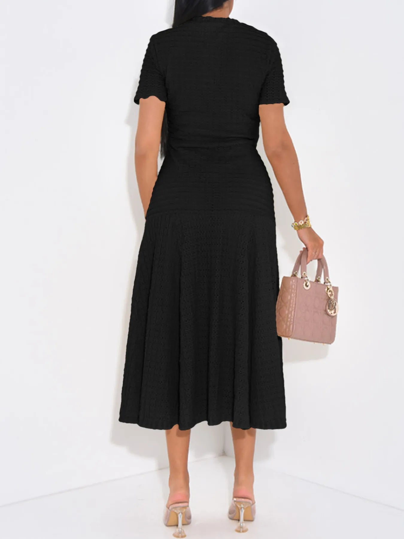 Back view of woman wearing a black Textured Knit Short Sleeve Midi Dress  holding a pink handbag on a white background