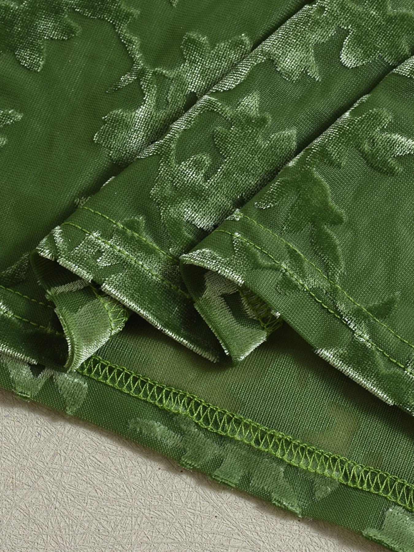 Close-up of green fabric hem  for Textured Tie-Front Bodycon Cami Dress on a light gray background