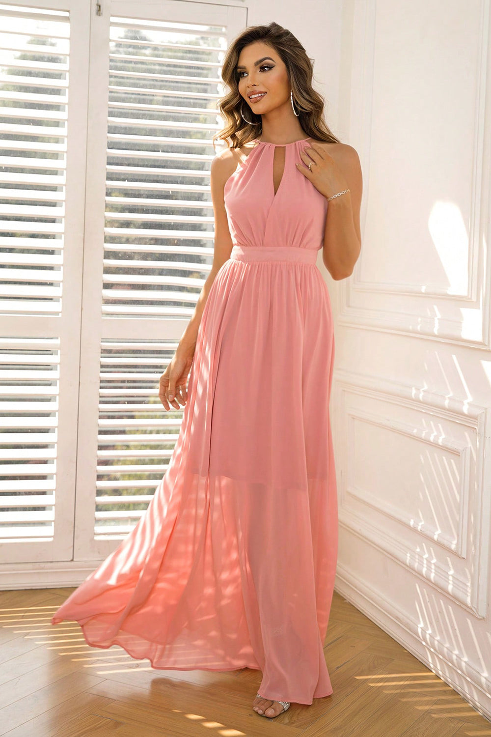 Model walking in a coral  sleeveless ruched maxi dress with halter neck and cutout front