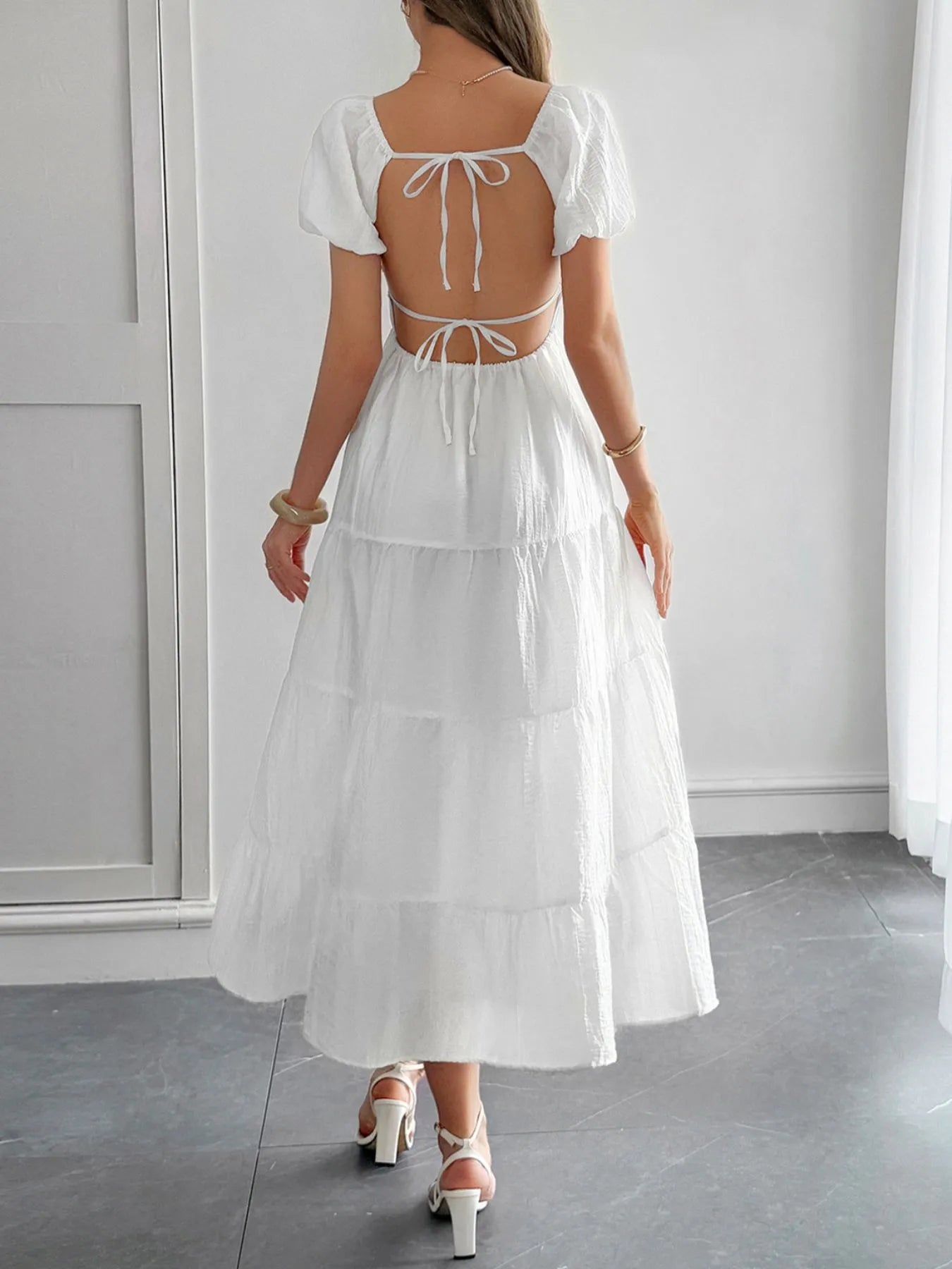 Back view of woman wearing a white backless summer Midi Dress with Short Sleeves with an open back in a minimal indoor setting