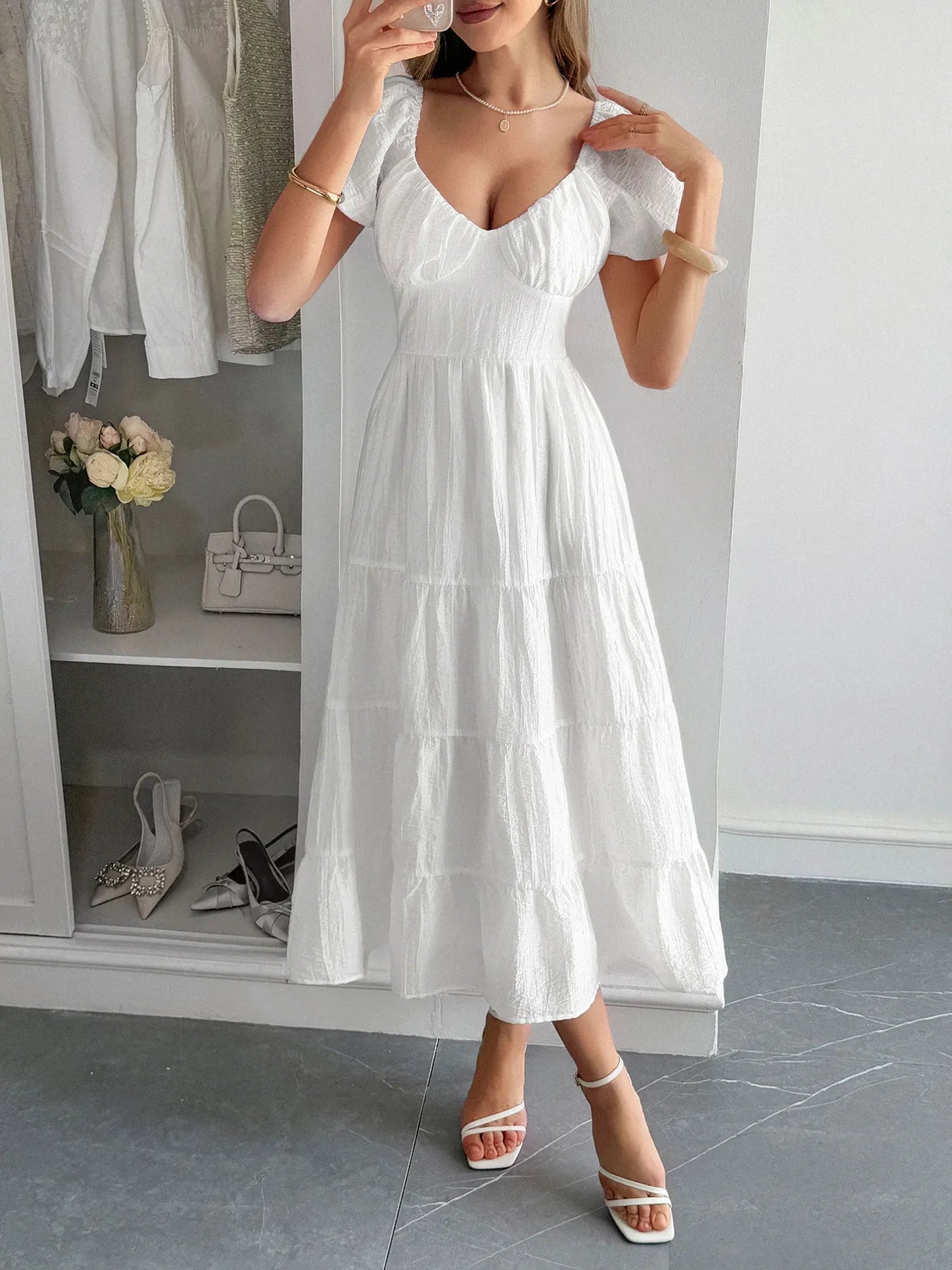 Woman wearing a white V-Neck open back Midi Dress with Short Sleeves in a room with shelves and shoes.