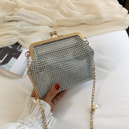 Hand holding silver rhinestone evening bag with gold pearl chain strap