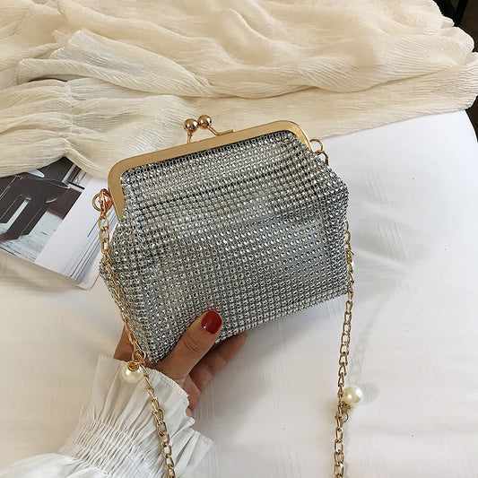 Hand holding silver rhinestone evening bag with gold pearl chain strap