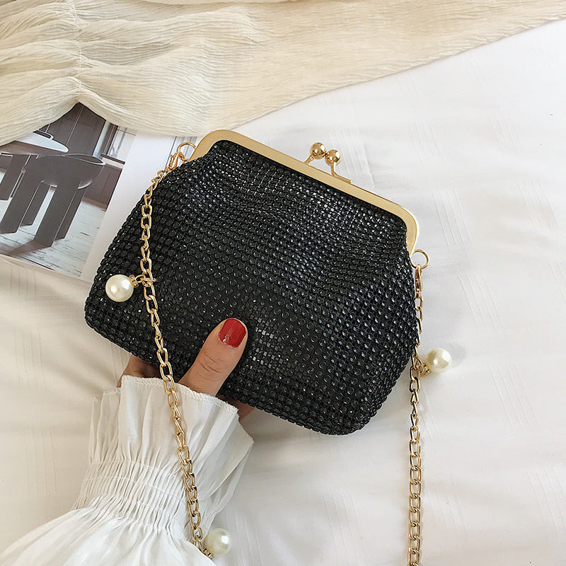 Hand holding black rhinestone evening bag with gold pearl chain strap