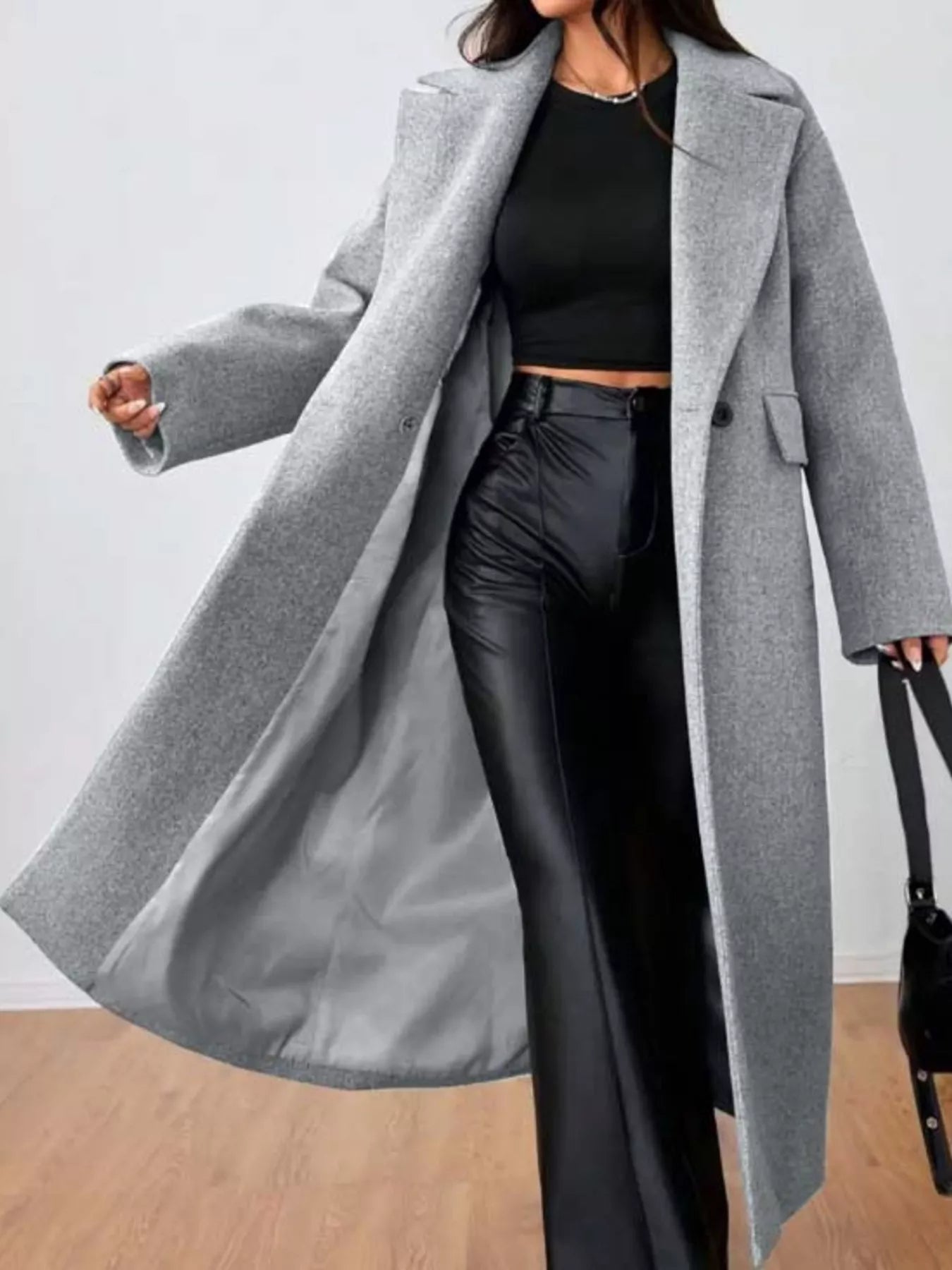 woman wearing a long gray coat over a black outfit on a plain background
