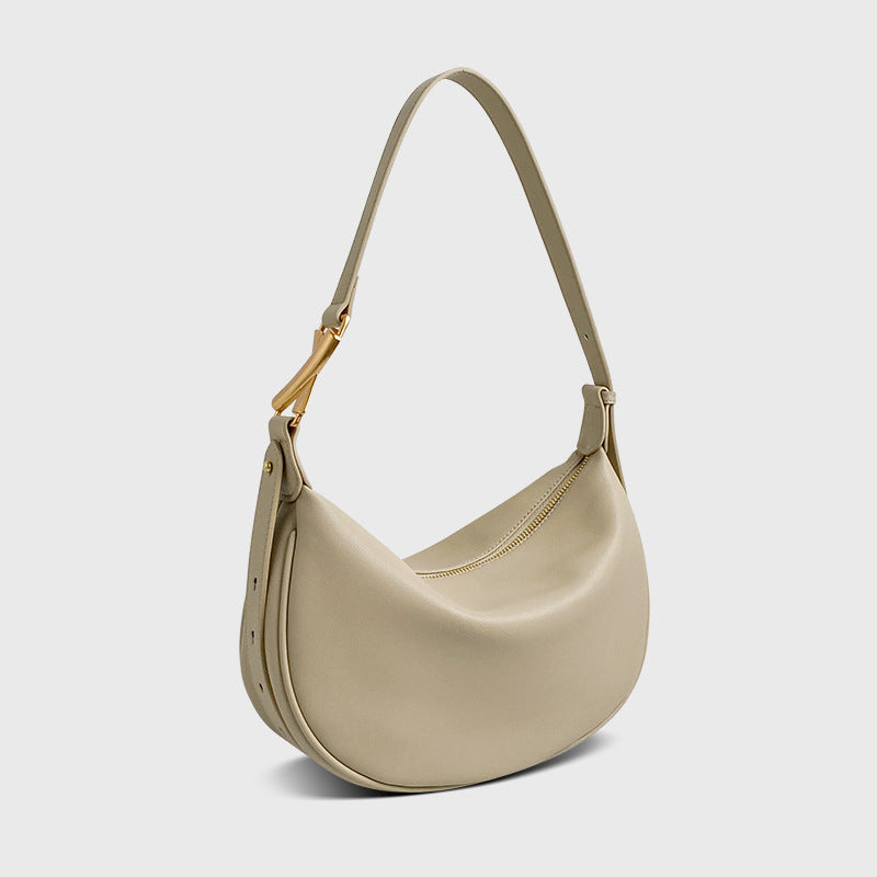A beige crescent-shaped genuine leather handbag with an adjustable strap and a zipper top closure.