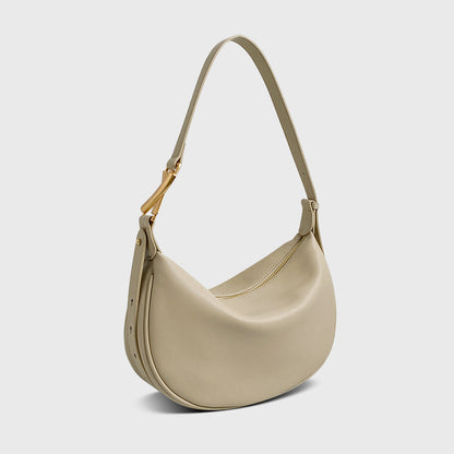 A beige crescent-shaped genuine leather handbag with an adjustable strap and a zipper top closure.