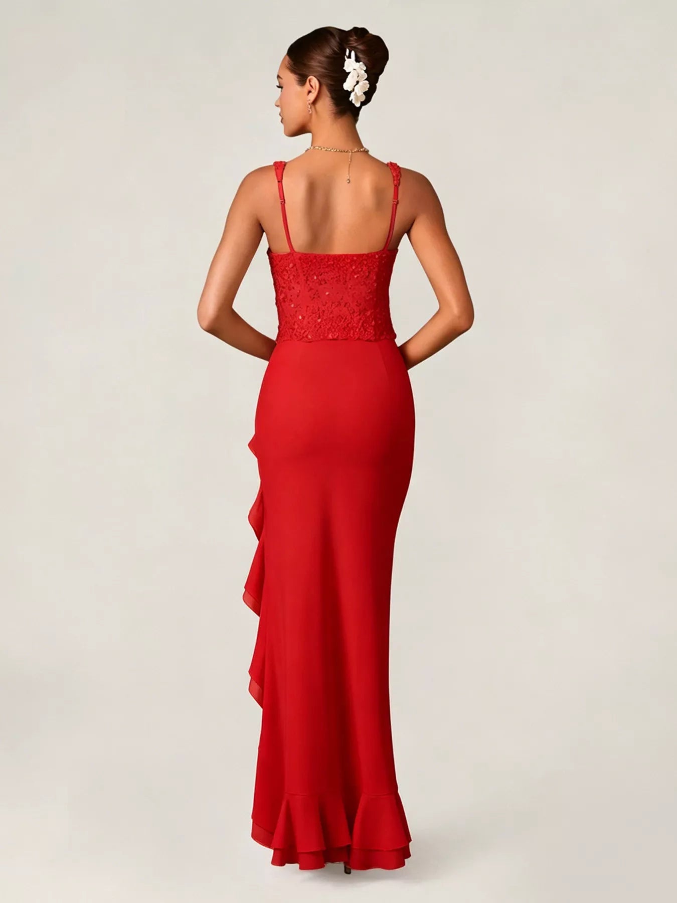 Woman wearing a black evening gown with sequin detailing top and ruffled skirt on a white background back view