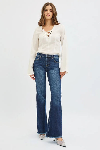 Model posing in dark wash blue denim mid rise flare leg tummy control jeans with frayed bottoms